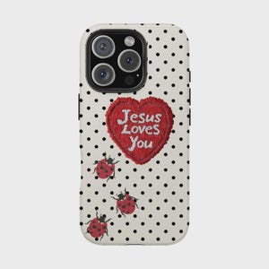 K&ouml;nnte beinhalten: Eine Handyh&uuml;lle mit wei&szlig;em Hintergrund und schwarzen Punkten. Ein rotes Herz mit dem gestickten Text "Jesus Loves You" ist auf der H&uuml;lle zentriert. Drei Marienk&auml;fer-Illustrationen sind ebenfalls abgebildet.