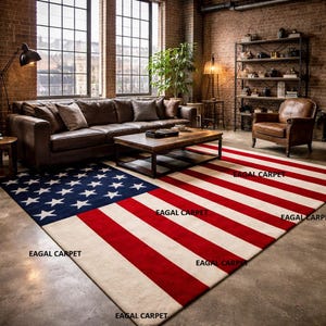 Op de afbeelding: Een rechthoekig vloerkleed met het ontwerp van de Amerikaanse vlag. Het vloerkleed heeft een blauw veld met witte sterren en rode en witte strepen. Het vloerkleed ligt in een woonkamer met een bruine leren bank en een houten salontafel.