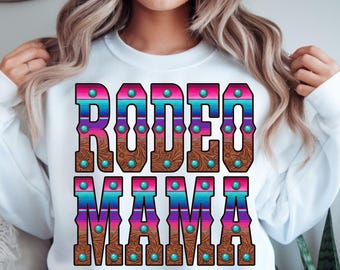 May include: White sweatshirt with the text "RODEO MAMA" in a colorful design. The letters are brown with a leather texture, turquoise studs, and a striped pattern in shades of pink, blue, and purple.