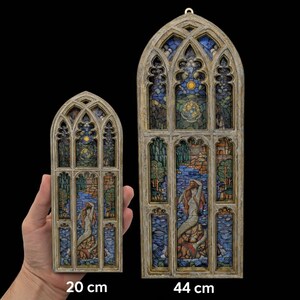 Może przedstawiać: Dwa dekoracyjne panele witrażowe. Większy panel ma 44 cm wysokości, mniejszy 20 cm. Oba przedstawiają scenę z syreną w odcieniach niebieskiego, zielonego i pomarańczowego, osadzoną w szczegółowej architektonicznej ramie.