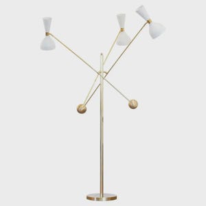 Könnte beinhalten: Eine moderne Stehlampe mit einem goldfarbenen Metallrahmen und vier weißen, kegelförmigen Lampenschirmen. Die Lampe hat einen kreisförmigen Sockel und eine Reihe sich kreuzender Arme, die sich von einer zentralen Stange erstrecken. Die Lampenschirme sind mit goldfarbenen Details versehen.
