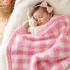 May include: A sleeping baby wrapped in a pink and white checkered blanket, clutching a stuffed bunny. The baby wears a pink bow headband. The blanket is soft and textured, creating a cozy and comforting scene.