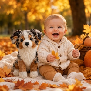 May include: A smiling baby wearing a cream-colored hooded sweater and brown pants sits on a blanket surrounded by autumn leaves. A crocheted dog with brown, white, and black details sits beside the baby. Pumpkins and a basket are in the background.
