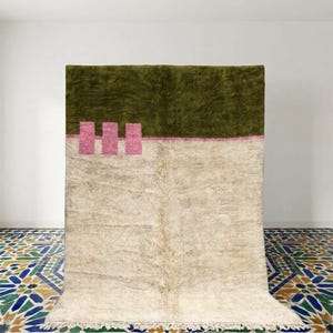 Puede incluir: Una alfombra rectangular que presenta un gran bloque de color verde oliva oscuro en la mitad superior y una mitad inferior de color crema. Una línea horizontal con tres acentos rectangulares rosas verticales separa los dos colores.