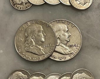 Puede incluir: Una colección de monedas de plata, incluyendo dimes y medios dólares, dispuestas sobre una superficie clara. Las monedas muestran retratos e inscripciones, con fechas visibles como 1965 y 1958. La palabra "LIBERTY" es visible en algunas monedas.