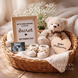 May include: A wicker basket holds a teddy bear, baby booties, a framed announcement reading "We've been keeping a little secret September 2026," an ultrasound image, and a wooden heart that says "Baby Williams."
