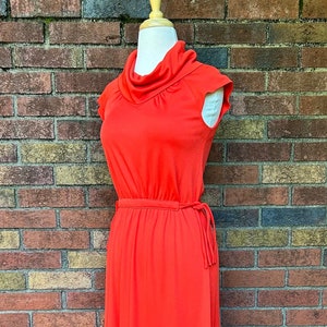 May include: A long, red maxi dress with a cowl neck and short sleeves. The dress has a tie at the waist.