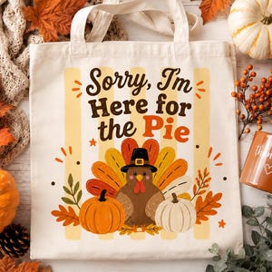 Puede incluir: Una bolsa de tela color crema con un gráfico de un pavo con sombrero de peregrino, flanqueado por dos calabazas. El texto dice, Sorry, I'm Here for the Pie. El diseño incluye hojas de otoño y rayas verticales amarillas en la tela.
