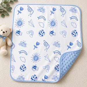Puede incluir: Una manta rectangular para bebé con base blanca y un patrón repetitivo de bocetos azules de flores, caracoles, mariposas, soles, aviones de papel, nubes, arcoíris, orugas y mariquitas, con un borde azul claro y reverso texturizado.