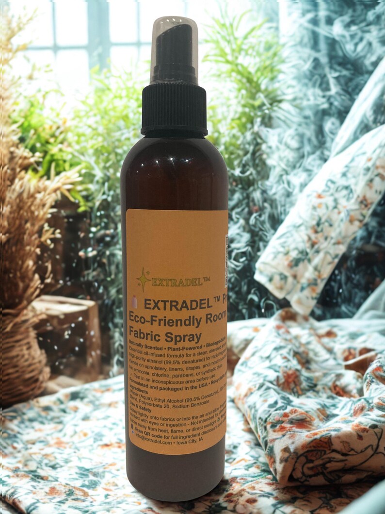 May include: A brown bottle of EXTRADEL Eco-Friendly Room Fabric Spray with a black spray nozzle. The label features text and a starburst design. The background includes greenery and patterned fabric.