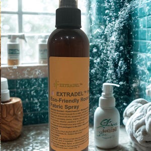 May include: A brown bottle of EXTRADEL Eco-Friendly Room Fabric Spray with a black spray nozzle and a tan label. The label includes product information. A white bottle with a pump dispenser is to the right.