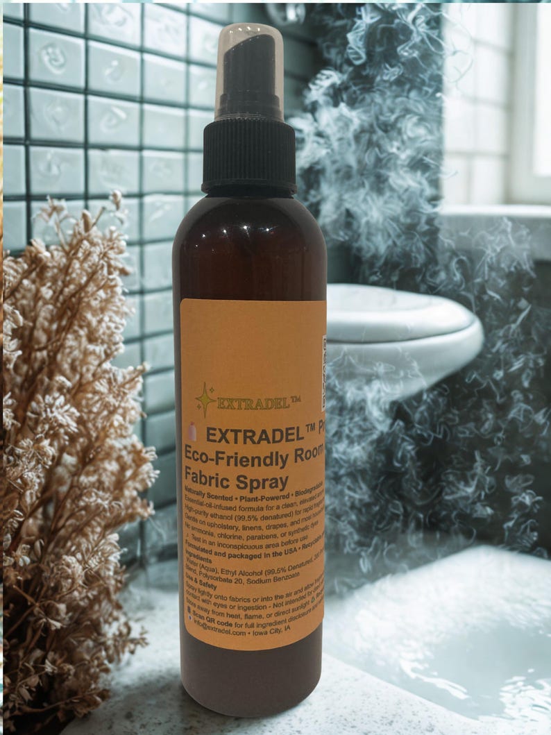 May include: A brown spray bottle with a black nozzle and a clear cap. The bottle has a tan label with the text "EXTRADEL Eco-Friendly Room Fabric Spray". The background shows a bathroom setting with a toilet and tile.