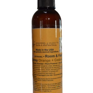 May include: A brown plastic spray bottle with a black nozzle and a yellow label. The label features the text EXTRADEL, Room & Fabric Spray Orange + Cedar, Made in the USA with globally sourced ingredients, and additional product safety information.