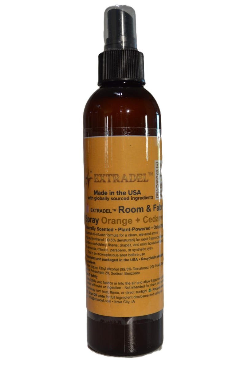 May include: A brown plastic spray bottle with a black nozzle and a yellow label. The label features the text EXTRADEL, Room & Fabric Spray Orange + Cedar, Made in the USA with globally sourced ingredients, and additional product safety information.