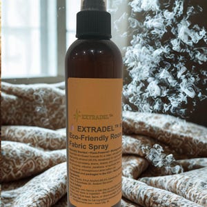May include: A brown spray bottle with a black nozzle and a tan label. The label reads "EXTRADEL Eco-Friendly Room Fabric Spray." The bottle is on a patterned fabric background. The spray bottle is designed for use on upholstery, linens, and drapes.
