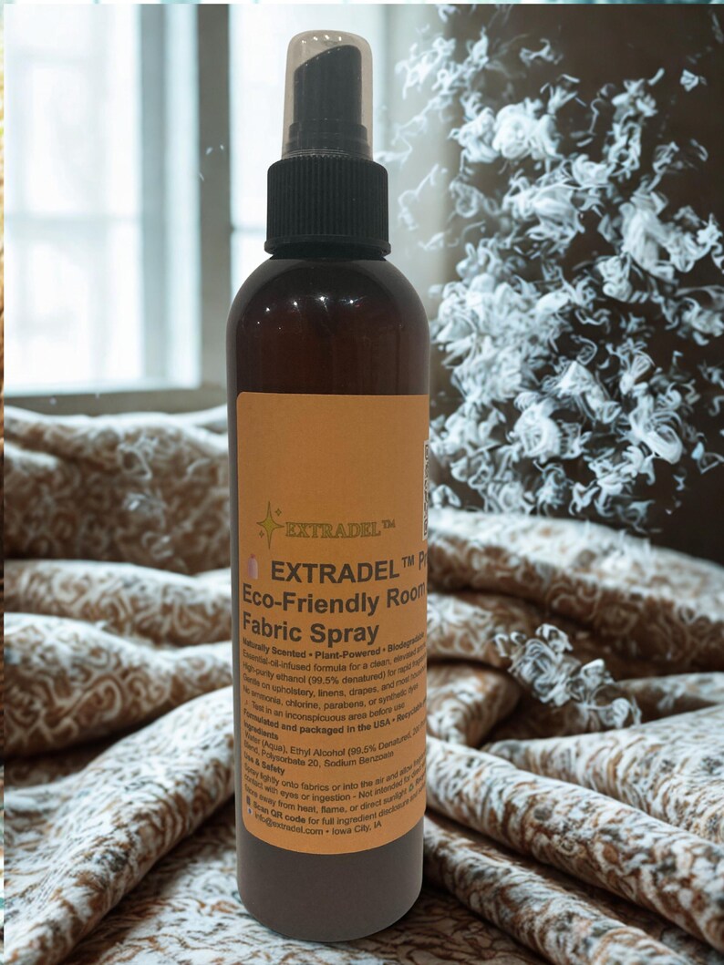 May include: A brown spray bottle with a black nozzle and a tan label. The label reads "EXTRADEL Eco-Friendly Room Fabric Spray." The bottle is on a patterned fabric background. The spray bottle is designed for use on upholstery, linens, and drapes.