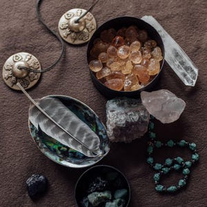 a collection of various crystals, gemstones, and jewelry arranged on a brown surface.