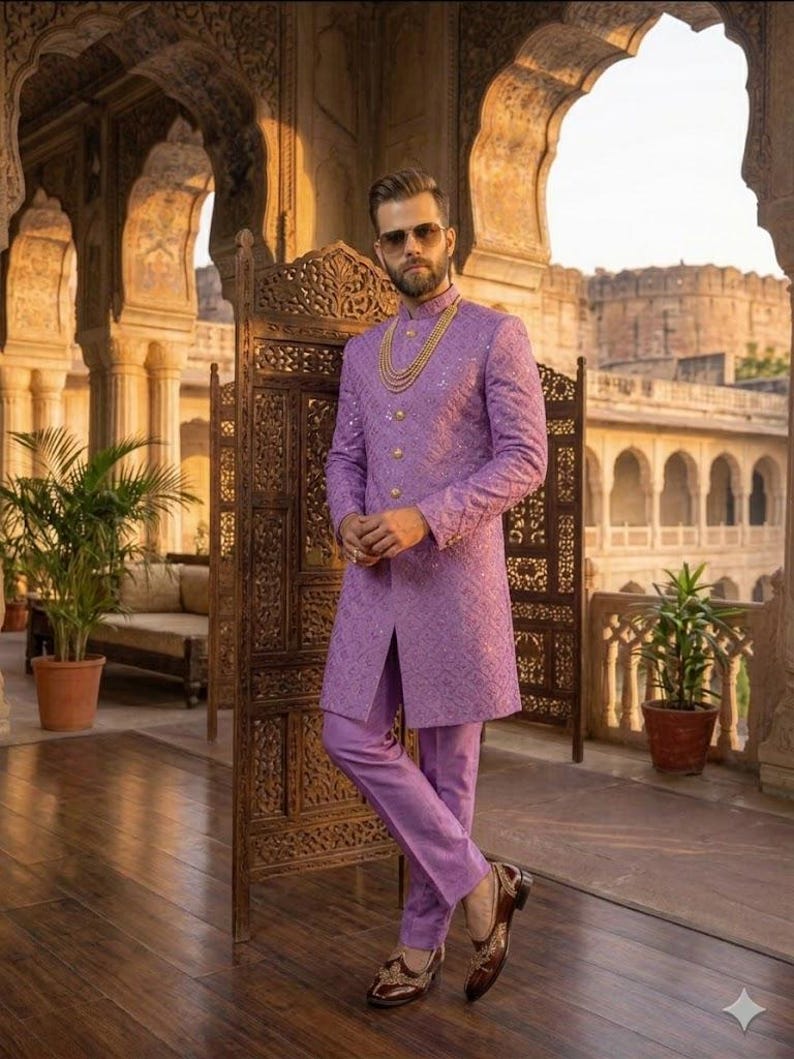 May include: A lilac suit comprising a long jacket and trousers. The jacket features a textured design and gold buttons. The outfit is complemented by brown leather shoes and a gold necklace. The background includes an ornate wooden screen and architectural features.