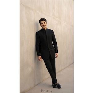 May include: A solid black bandhgala suit featuring a long-sleeved jacket with a high mandarin collar and matching slim-fit trousers. The jacket has a concealed front placket and a clean, structured silhouette. The ensemble is paired with black loafers.