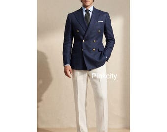 Puede incluir: Un blazer azul marino de doble botonadura con botones dorados, una camisa de cuello azul claro, una corbata oscura estampada y pantalones blancos. El conjunto se completa con zapatos de cuero marrón. El texto Pinkcity es visible.