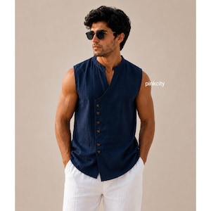 Puede incluir: Una camisa sin mangas de color azul marino con cuello mao y una tapeta frontal asimétrica que presenta una hilera de botones oscuros. La camisa tiene un acabado de tela texturizada y se combina con pantalones blancos. El texto pinkcity es visible a la derecha.
