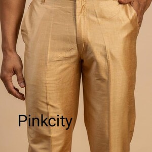 May include: Gold-colored trousers with a slight sheen, featuring a button closure and pockets. The text "Pinkcity" is printed at the bottom of the image. The pants appear to be made of a smooth, possibly silk-like fabric.