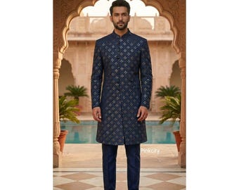 May include: A dark blue sherwani featuring a repeating gold diamond pattern, a high mandarin collar, and a full-length button-down front. The garment is paired with matching dark blue trousers and dark blue loafers, creating a cohesive ensemble.