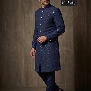 May include: A navy blue sherwani featuring intricate tonal embroidery and small reflective mirror accents throughout. The garment has a high mandarin collar, a front button placket with four light-colored buttons, and long sleeves. The text Pinkcity is visible.