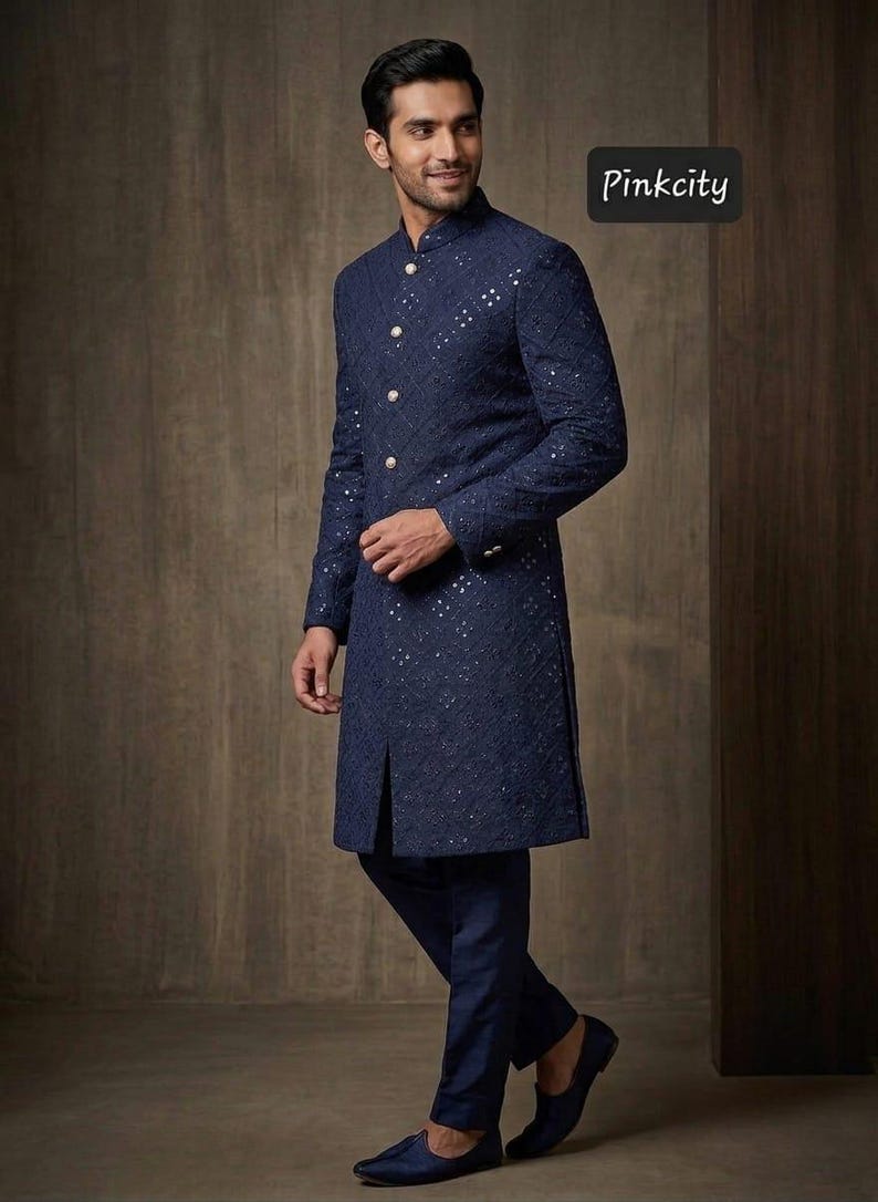 May include: A navy blue sherwani featuring intricate tonal embroidery and small reflective mirror accents throughout. The garment has a high mandarin collar, a front button placket with four light-colored buttons, and long sleeves. The text Pinkcity is visible.