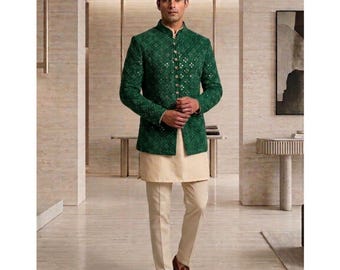 May include: Emerald green jacket with a high collar and intricate detailing, paired with a cream-colored tunic and trousers. The jacket features a diamond pattern and small embellishments. The outfit is completed with brown leather loafers. The image is set in a modern interior.