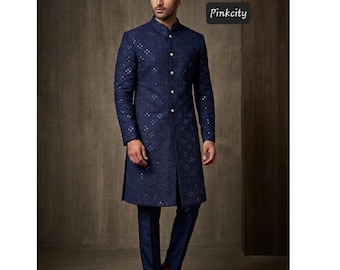 May include: A dark blue sherwani featuring a mandarin collar, long sleeves, and a front button placket. The garment is adorned with an all-over intricate tonal embroidery pattern and small reflective mirror accents. The text Pinkcity is visible.