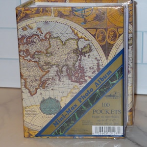 May include: A photo album with a vintage map design. The album is wrapped in plastic and features a blue and gold diagonal banner with the text "Mini-Max Photo Album". The album holds 100 pockets for photos up to 4" x 6".
