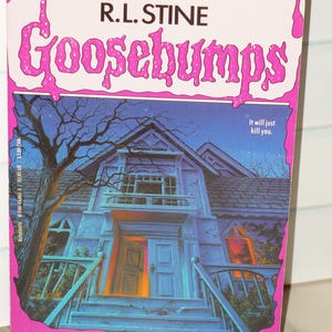 May include: A paperback book titled Goosebumps: Welcome to Dead House by R.L. Stine. The cover features a blue-toned illustration of a house with an open door, surrounded by pink, dripping text and the phrase It will just kill you.