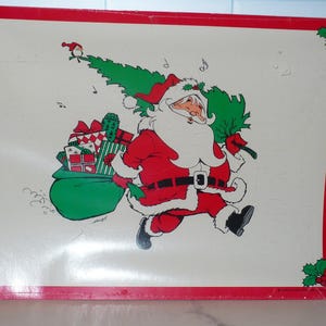 May include: A rectangular Christmas-themed tray with a red border and holly accents. The tray features a cartoon illustration of Santa Claus in a red suit, carrying a green sack of gifts and a Christmas tree.