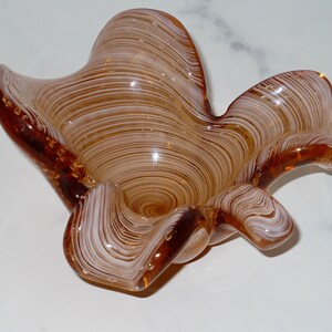 May include: A decorative glass bowl with a unique, organic shape. The bowl features a swirling pattern of brown and white, with a glossy finish. The bowl has a petal-like design and is suitable for home decor.