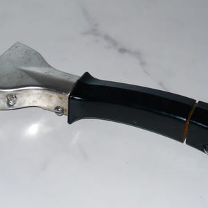 May include: A silver and black pot handle with a hook on the end. The handle is made of metal and has a black plastic grip.
