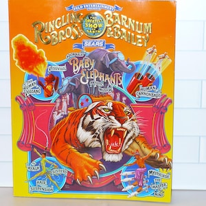May include: A vintage Ringling Bros. and Barnum & Bailey Circus poster. The orange and yellow poster features a roaring tiger, elephants, and circus performers. Text includes "The Greatest Show on Earth" and "Baby Elephants".