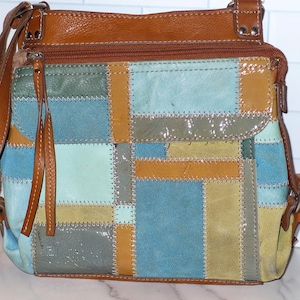 May include: A brown leather crossbody bag with a patchwork design in shades of blue, green, and tan. The bag has a brown leather strap and a zippered top. The front flap has two brown leather tassels.