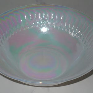 May include: A white iridescent glass bowl with a scalloped edge and a wavy pattern. The bowl is made of opal glass and has a pearlescent finish.