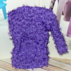 May include: A purple long-sleeved shirt with a fuzzy texture. The shirt has a sparkly, iridescent finish.