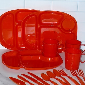 May include: A set of orange plastic dinnerware, including two divided plates, four cups, four forks, four spoons, and four knives.