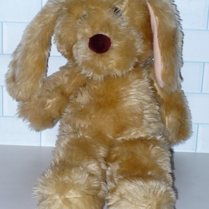 May include: A plush brown dog toy with floppy ears. The dog has a burgundy nose and pink inner ears.