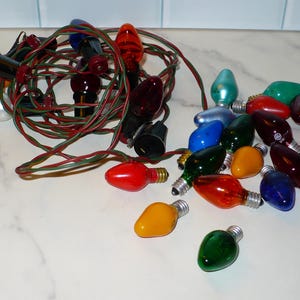 May include: A collection of colorful Christmas lights with red, green, yellow, blue, and orange bulbs. The lights are strung together with green and red wires, creating a festive display.