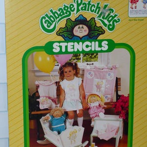 May include: A yellow Cabbage Patch Kids stencil set package featuring two 8.5 inch by 11 inch pre-cut stencil sheets. The packaging displays a photograph of a child with dolls, a rocking cradle, and fabric items decorated with stencil designs.
