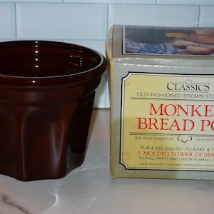 May include: A brown stoneware Monkey Bread Pot with a six-inch diameter, next to its original box. The box features the text "Monkey Bread Pot" and "Old-Fashioned Brown Stoneware."