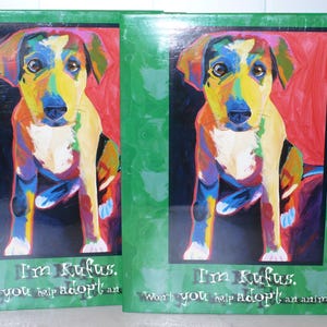 May include: Two green-framed art prints featuring a colorful painting of a dog. The dog is depicted with a vibrant palette of colors, including yellow, blue, and red. The text "I'm Rufus. Won't you help adopt an animal?" is at the bottom.