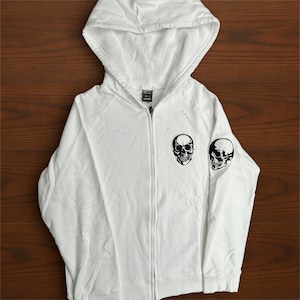 May include: A white ceramic mug with a black handle and the text "But First, Coffee" in a bold, black font. The mug is set against a blurred background, suggesting a cozy setting.