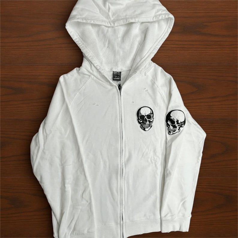 May include: A white ceramic mug with a black handle and the text "But First, Coffee" in a bold, black font. The mug is set against a blurred background, suggesting a cozy setting.