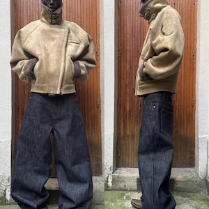 May include: A two-panel image shows a person wearing a tan suede jacket with a high collar and dark blue denim jeans. The jacket has a shearling lining and a diagonal zipper. The jeans are wide-legged and dark wash. Brown leather shoes complete the look.