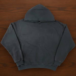 May include: A dark gray hoodie with a hood, long sleeves, and a ribbed hem and cuffs. The hoodie is made of a soft, comfortable material and is suitable for casual wear. The garment is displayed on a wooden surface.